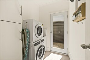 A laundry room with a washing machine and dryer, a door leading outside, and a small shelf with items on it. - Coral Haven ~ Port Willunga - Seaside Sanctuary in a Prime Port Willunga Location (Port Willunga)