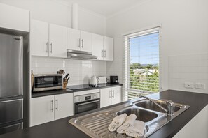 A modern kitchen with stainless steel appliances, white cabinetry, and a large window with a view. - Coral Haven ~ Port Willunga - Seaside Sanctuary in a Prime Port Willunga Location (Port Willunga)