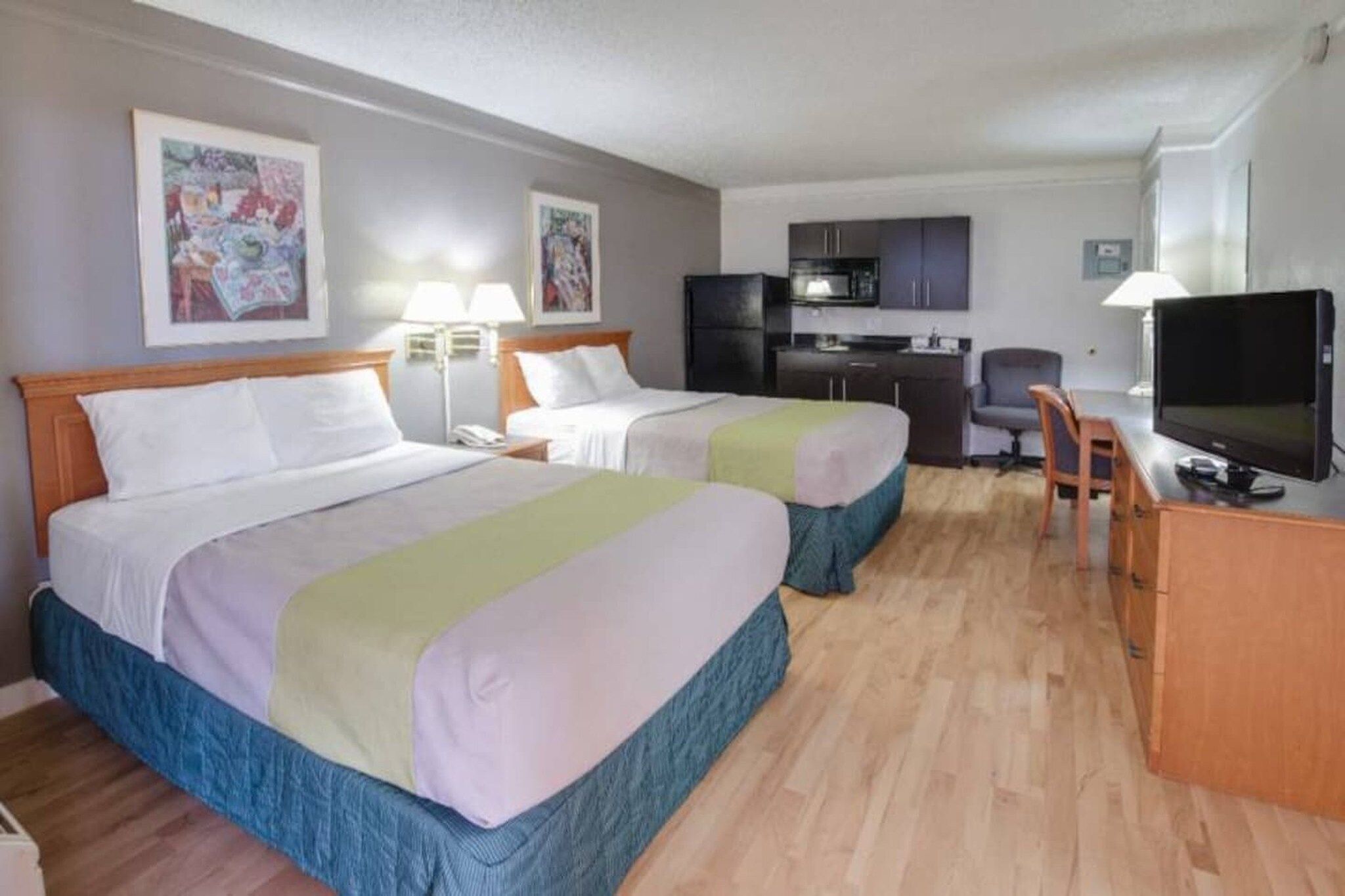 Een hotelkamer met twee bedden, een bureau, een stoel, een televisie en een kitchenette.
