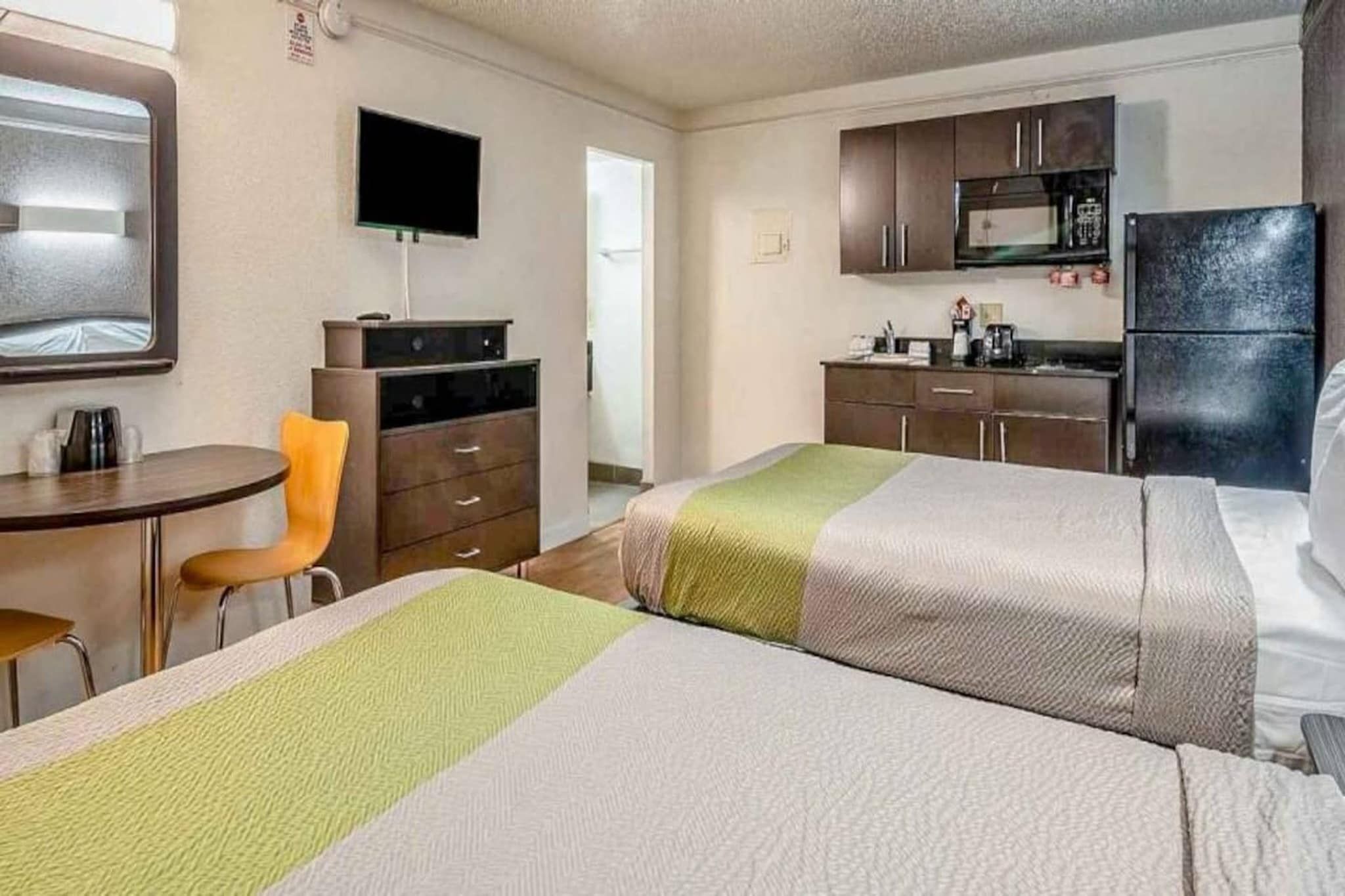 Een hotelkamer met twee bedden, een bureau, een stoel, een televisie, een kitchenette en een raam.