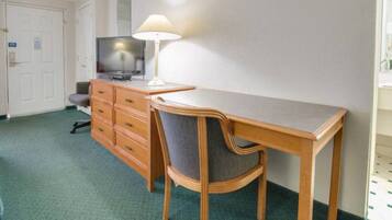Een hotelkamer met een houten bureau, een stoel, een televisie op een dressoir en een lamp.