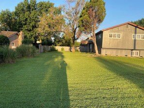 A residential backyard with a well-maintained lawn, a wooden fence, and a large tree. - KU Lake & Golf House (Pet Friendly) (Lawrence)