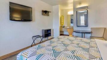 A hotel room with a bed, a television, a desk, a chair, a mirror, and a small shelf.