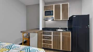 A compact kitchen with a microwave, stove, sink, and a black refrigerator.