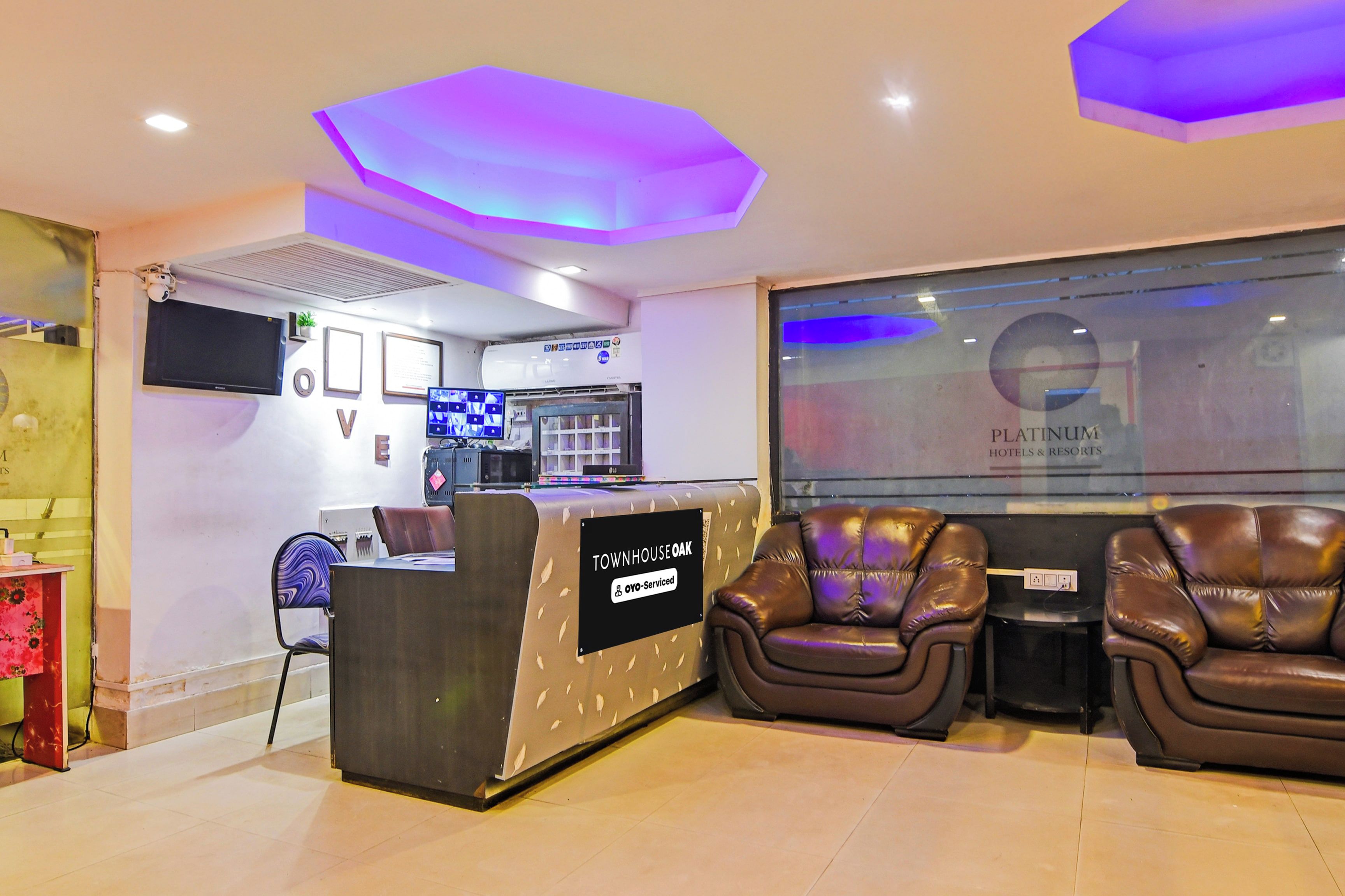 A reception area with a reception desk, seating area with leather chairs, a flat-screen TV, and a wall-mounted air conditioning unit.