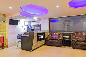 Zona de recepción con mostrador, área de estar con sillones de cuero, televisor de pantalla plana y aire acondicionado de pared.