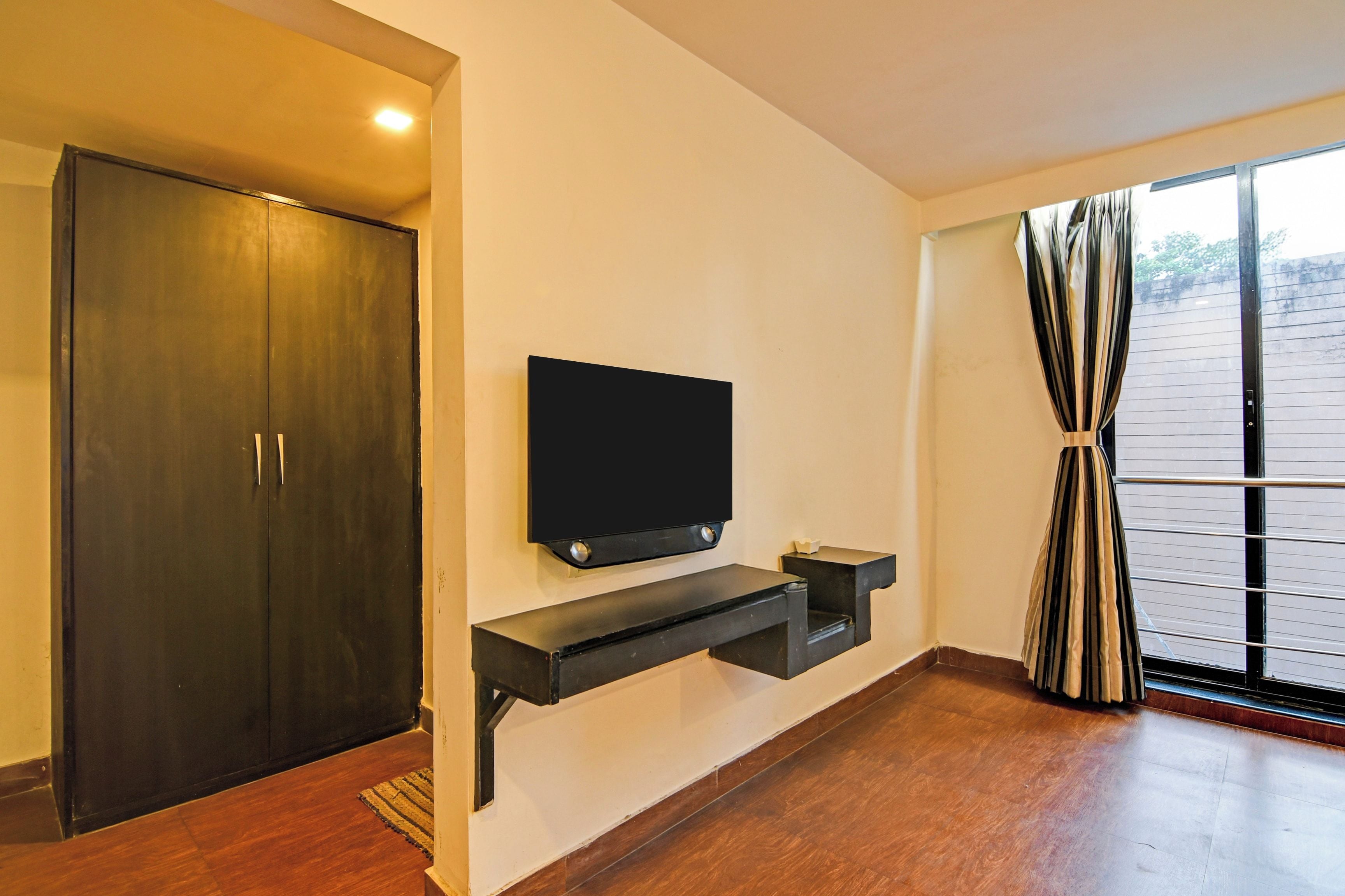 Ein Zimmer mit einem dunklen Holzschrank, einem Wand-Fernseher und einem Fenster mit Vorhängen.