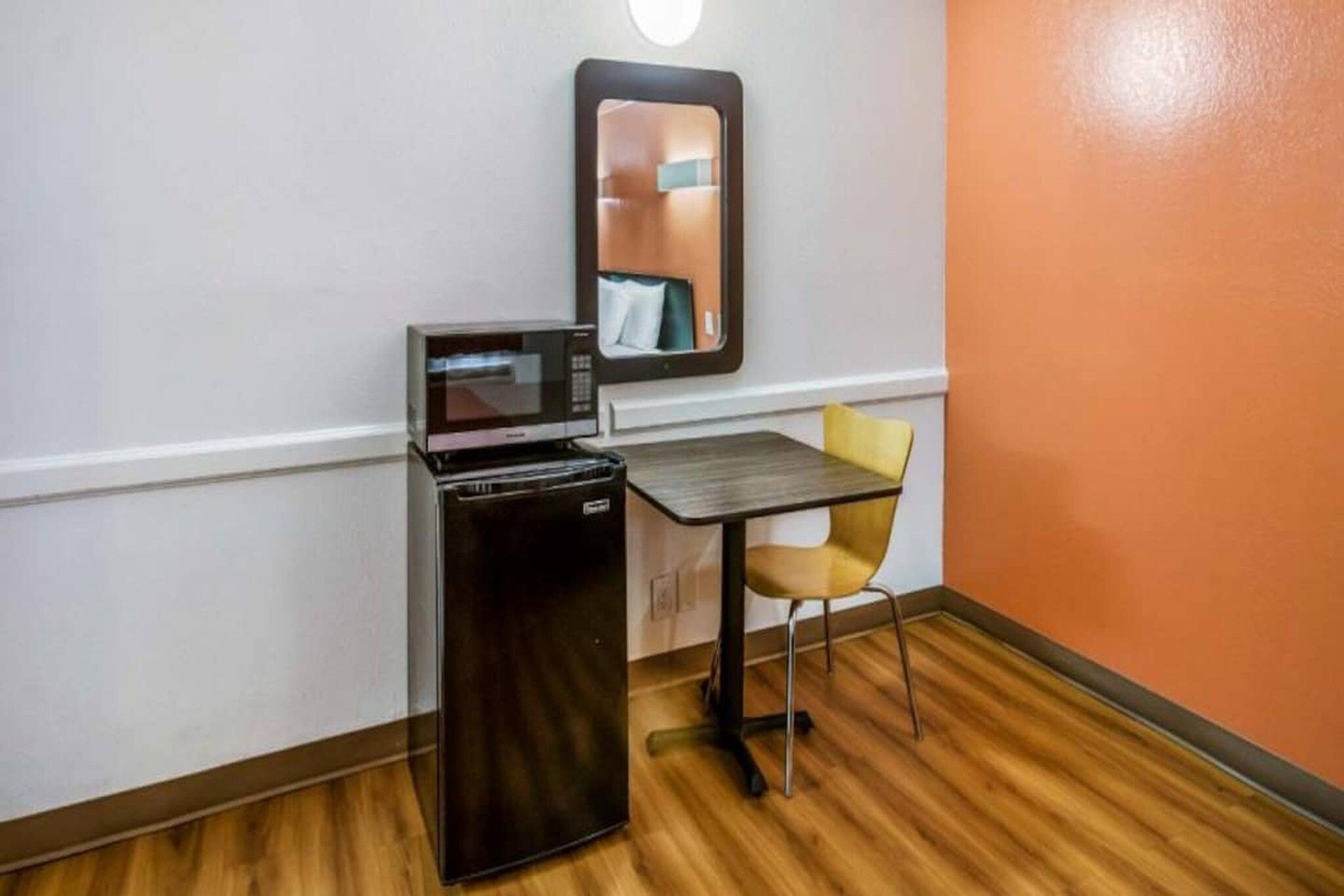 A compact room with a kitchenette, a small table, a chair, and a mirror on the wall.