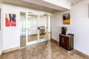 A hotel lobby with a reception desk, a glass door entrance, and a wall-mounted coffee machine. - Elegant 1 King Bed | Non-Smoking (EULESS)