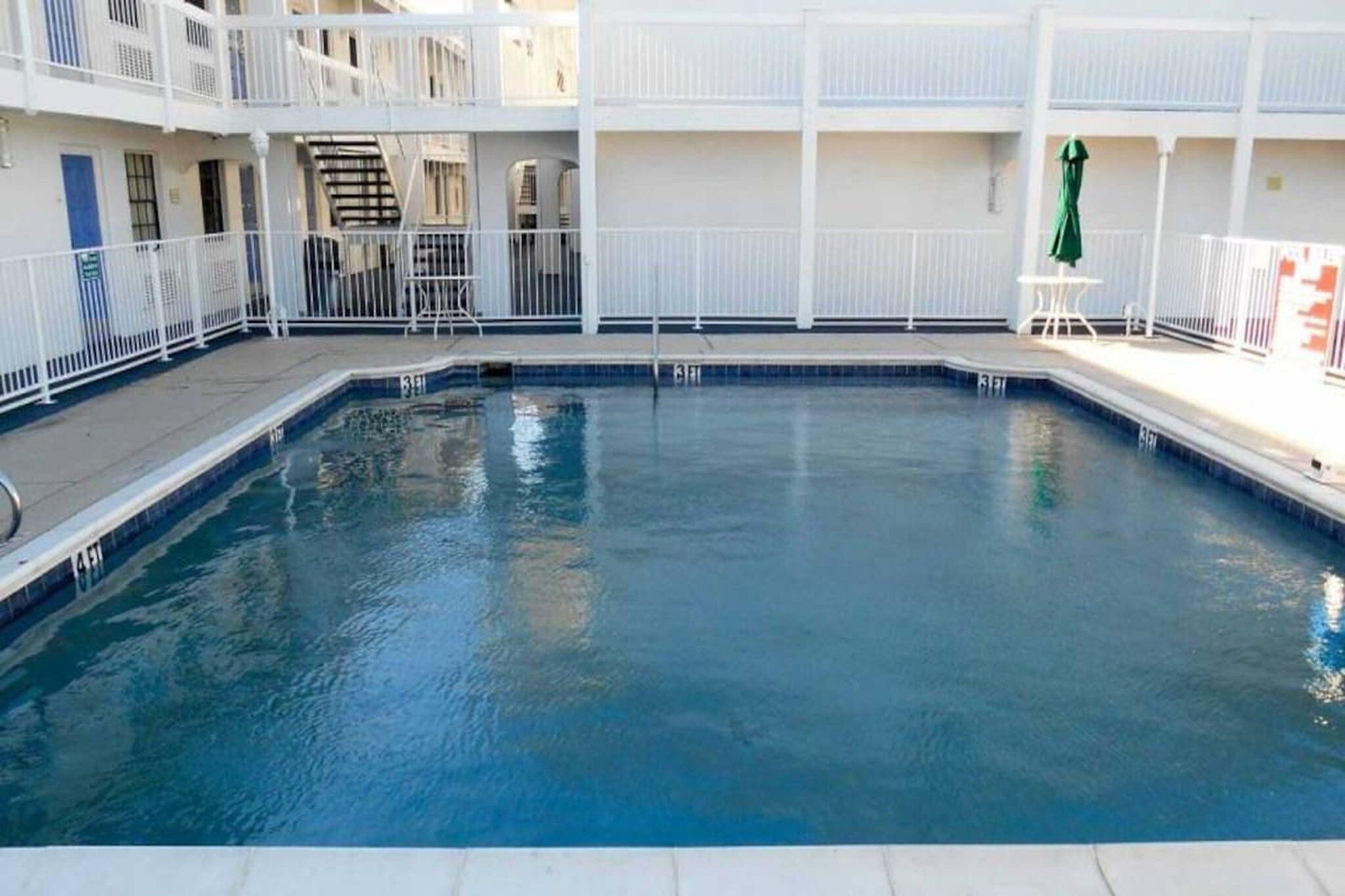 A swimming pool with a white surrounding deck and a multi-level building with balconies.
