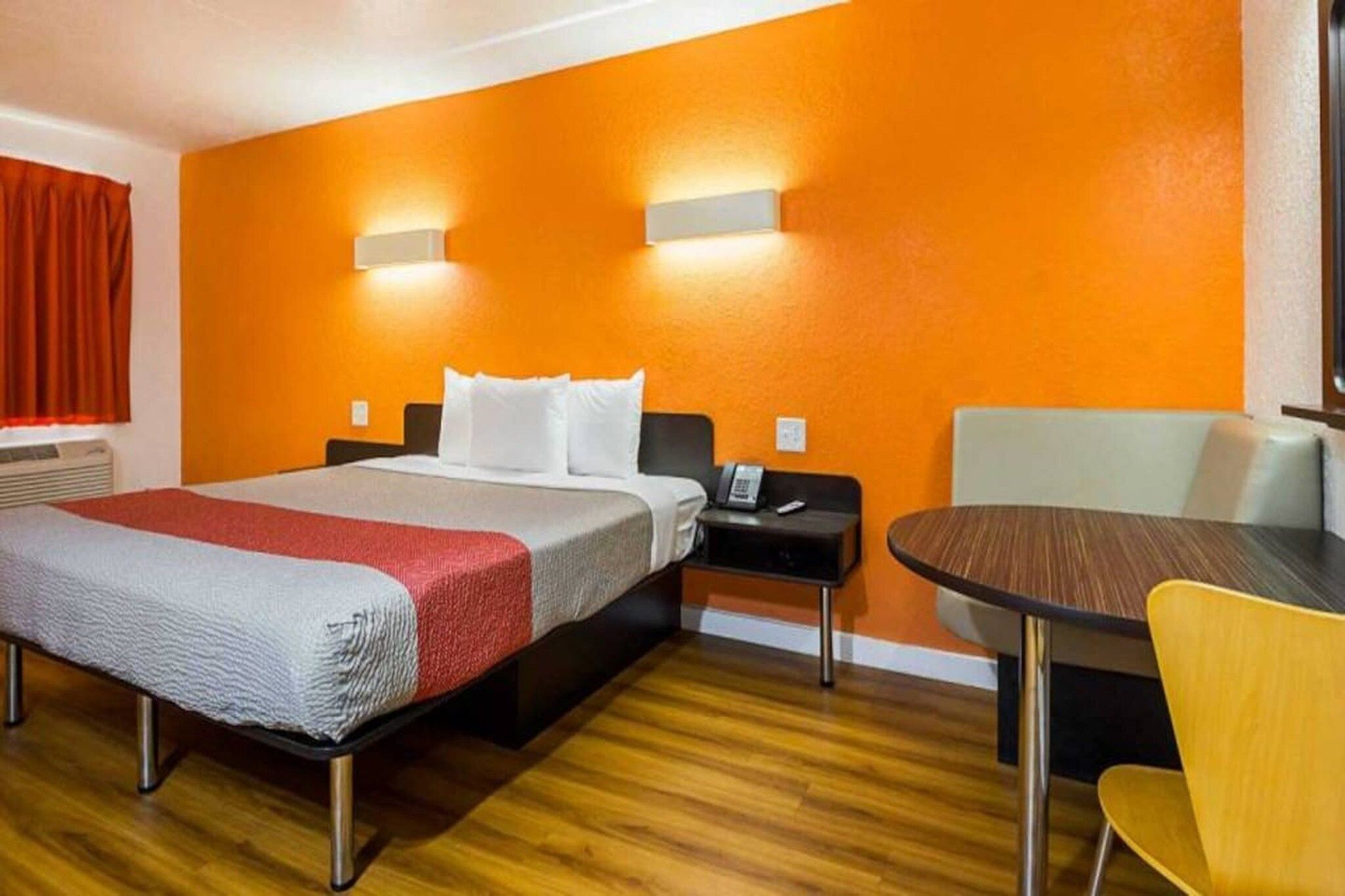 A hotel room with a bed, bedside table, chair, and a small table with a chair.