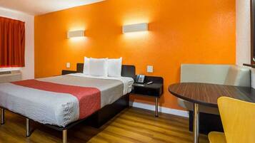 A hotel room with a bed, bedside table, chair, and a small table with a chair.