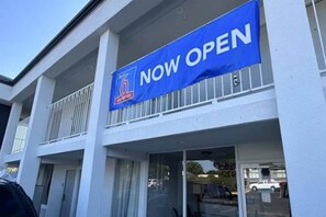 Un bâtiment sur lequel on peut lire une pancarte « OUVERT MAINTENANT », doté d’un balcon et d’une devanture avec des portes vitrées.