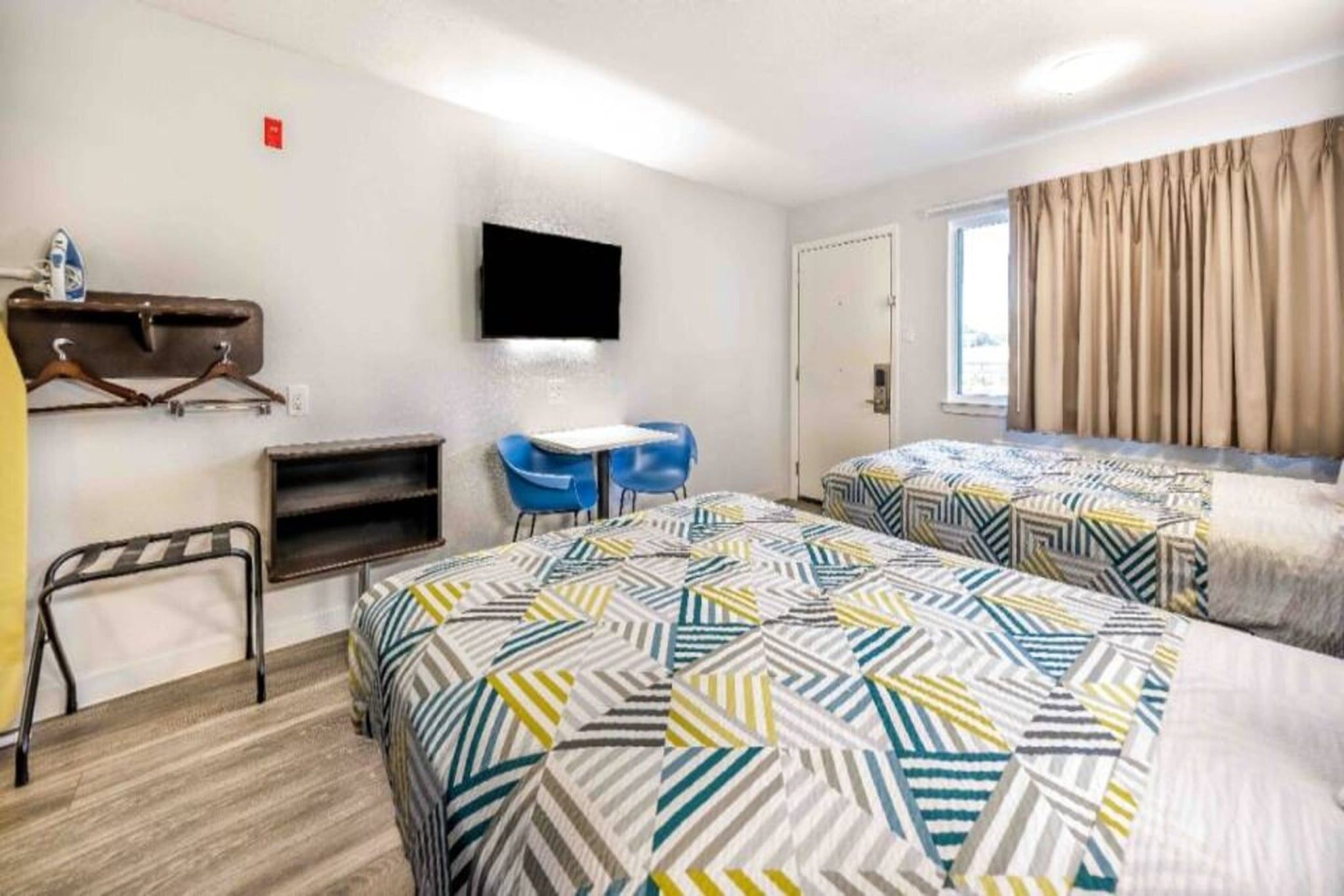 Ein Hotelzimmer mit zwei Betten, einem Schreibtisch, einem Sessel, einem Fernseher und einem Fenster mit Vorhängen.
