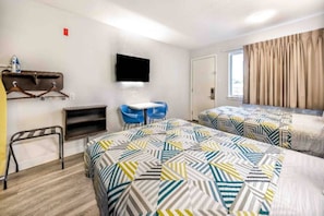 Ein Hotelzimmer mit zwei Betten, einem Schreibtisch, einem Sessel, einem Fernseher und einem Fenster mit Vorhängen.