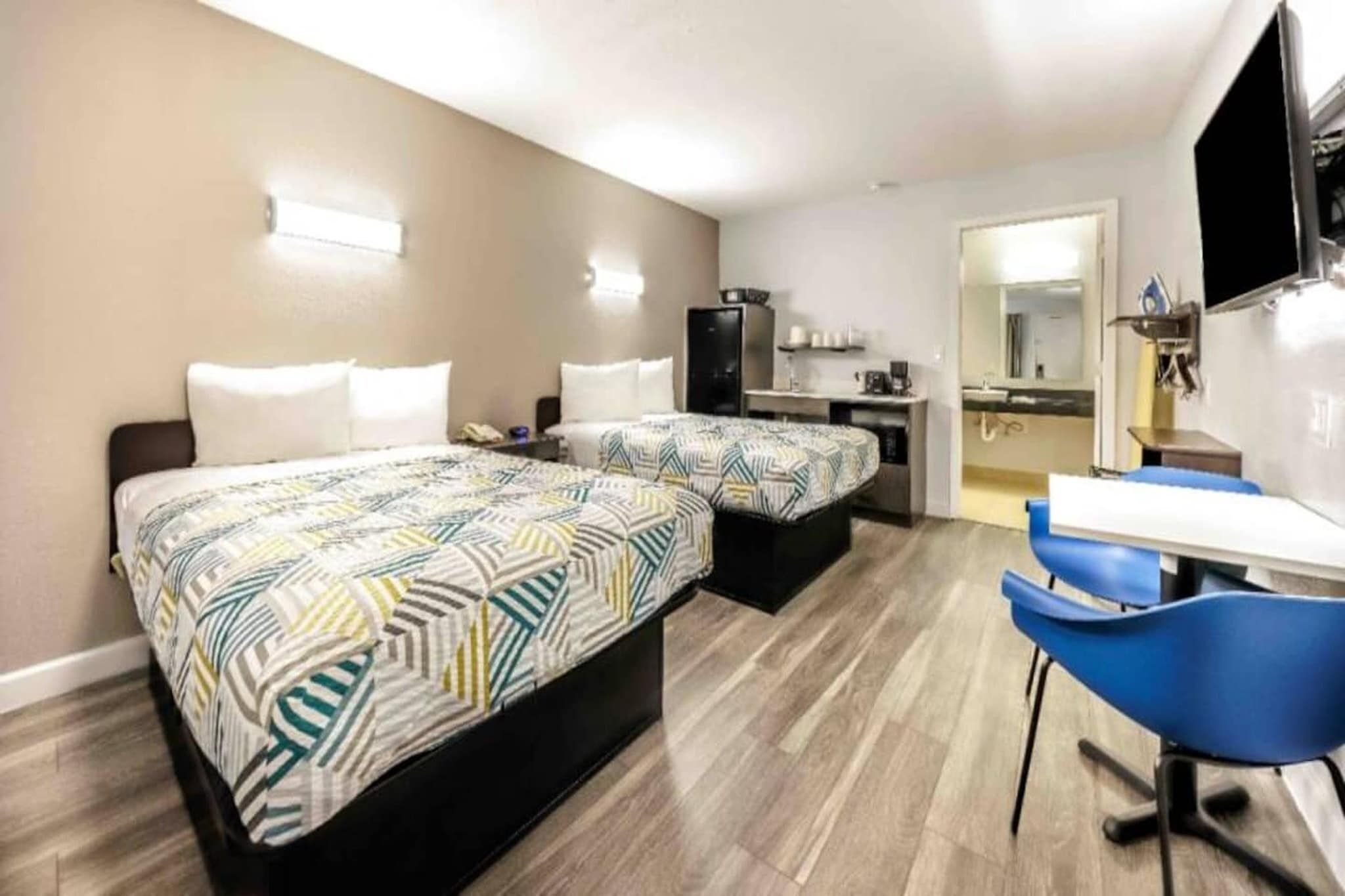 Hotellihuone, jossa on kaksi sänkyä, työpöytä, tuoli, televisio ja pieni keittiönurkkaus.