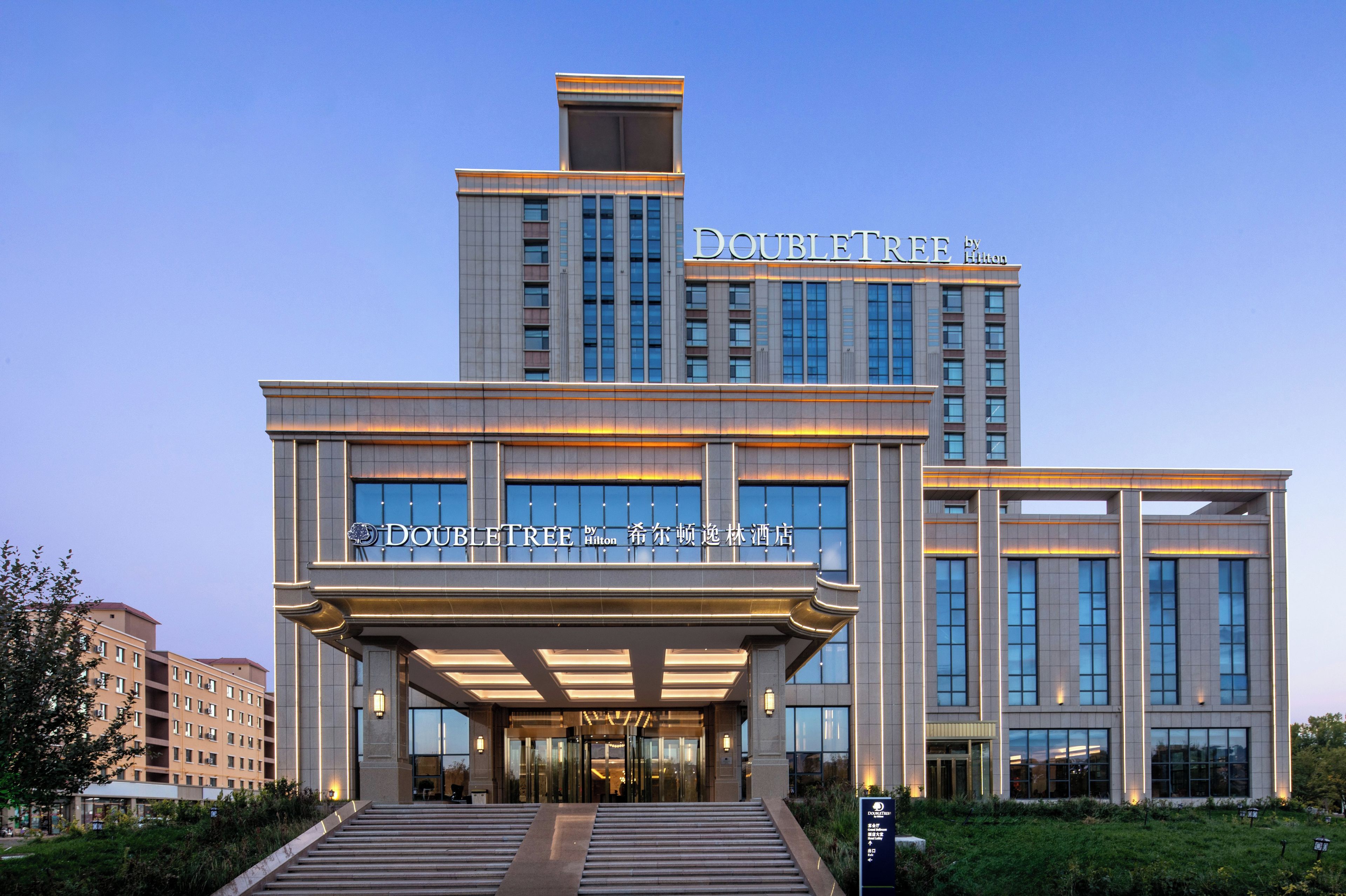 Ein modernes Hotelgebäude mit einem gut sichtbaren 'DOUBLETREE by Hilton' Schild, das eine symmetrische Fassade mit großen Fenstern und einem zentralen Eingang aufweist.