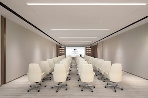 Un salón de conferencias con filas de sillas blancas, una pantalla grande al frente y un diseño de techo moderno.