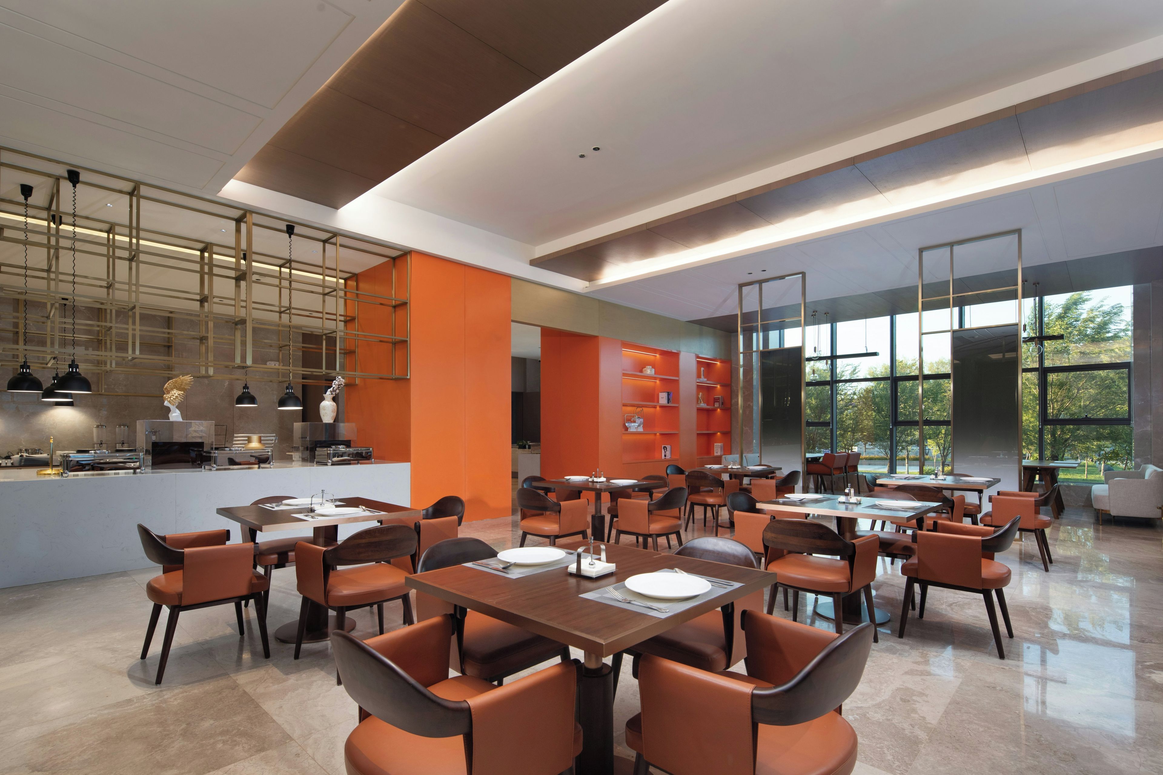 Un espace de restauration moderne avec plusieurs tables et chaises, une cuisine en arrière-plan et de grandes fenêtres qui laissent entrer la lumière naturelle.