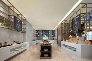 L’intérieur d’un café moderne, avec un sol en marbre, des étagères en métal et un comptoir central où se trouve le matériel nécessaire à la préparation du café.