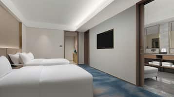 Ein Hotelzimmer mit zwei Betten, einem Flachbildfernseher, einem großen Spiegel und einem Badezimmer mit Handtüchern.