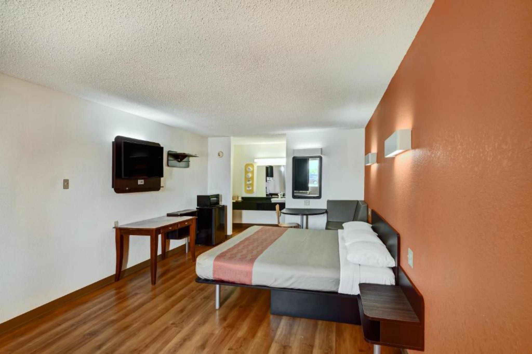 Habitación de hotel con cama, escritorio, silla, televisión y baño visible a través de una puerta abierta.