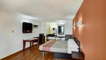 Habitación de hotel con cama, escritorio, silla, televisión y baño visible a través de una puerta abierta.