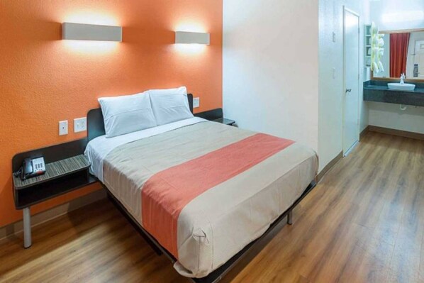 Une chambre d’hôtel avec un lit, une table de chevet et une salle de bain visible au fond.