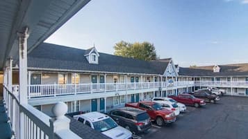 Un motel avec une rangée de chambres, chacune dotée d’un balcon et d’un petit porche. Un parking se trouve devant, où plusieurs voitures sont garées.