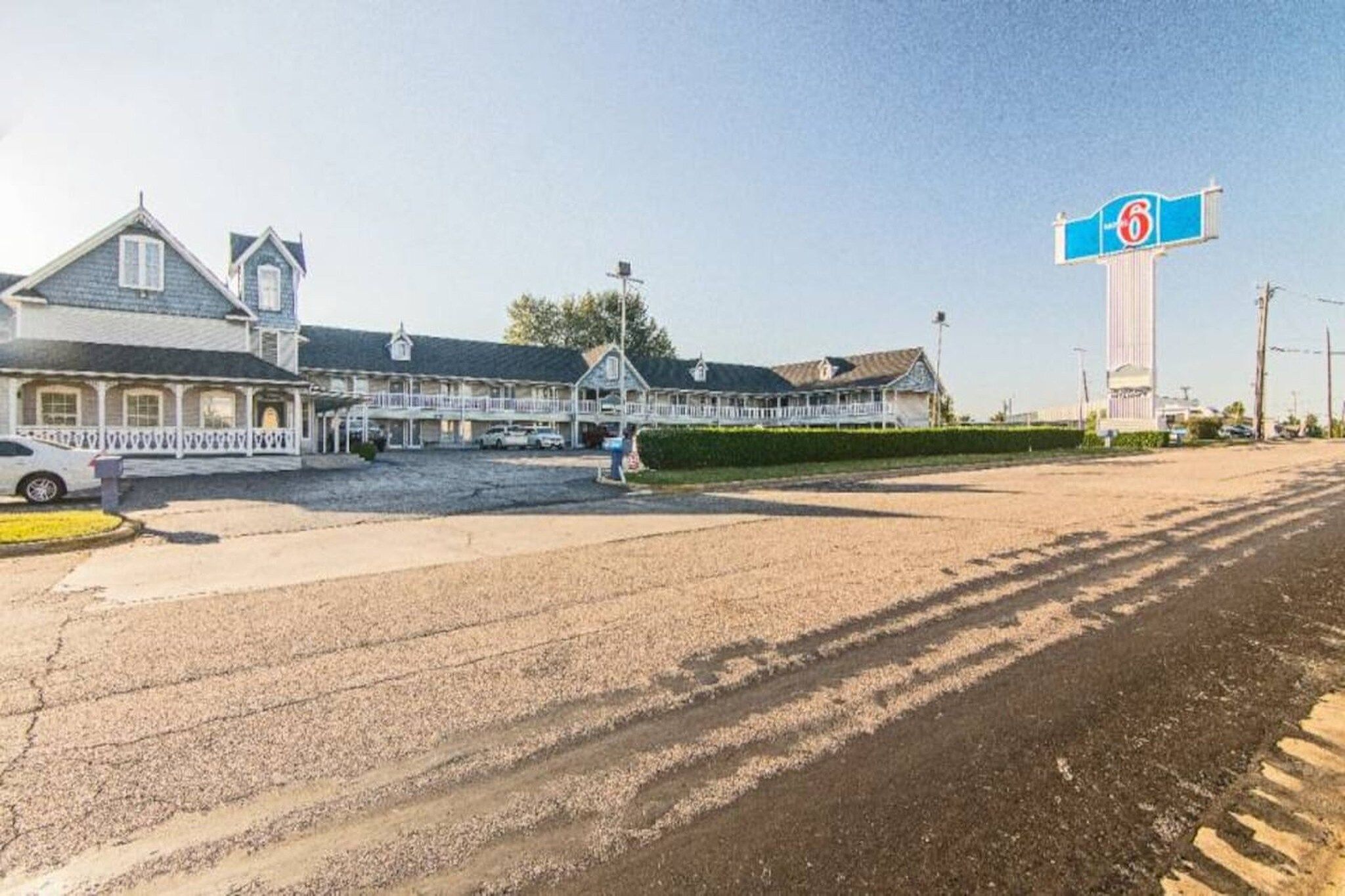 A motel with a large parking lot, a covered outdoor seating area, and a prominent sign indicating the number 6.