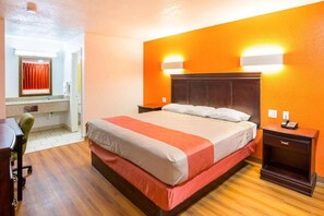 Ein Hotelzimmer mit Bett, Schreibtisch, Stuhl, Nachttisch und Wandlampe.