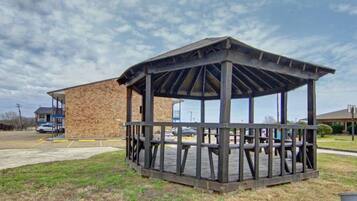 A gazebo with a wooden structure and a brick building in the background.
