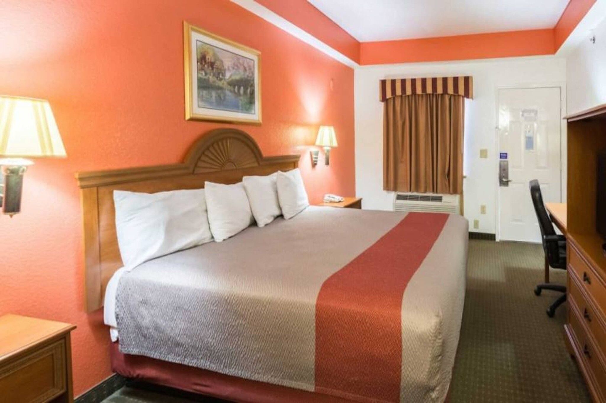 A hotel room with a bed, bedside lamps, a desk, and a door.