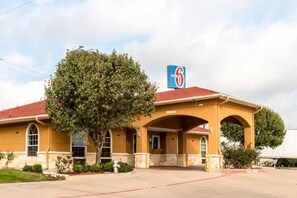 Un motel avec un toit rouge, un grand arbre devant et une enseigne avec le chiffre six.