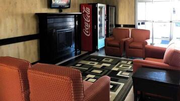 Un vestíbulo con chimenea, sillones rojos, alfombra estampada y un refrigerador Coca-Cola.