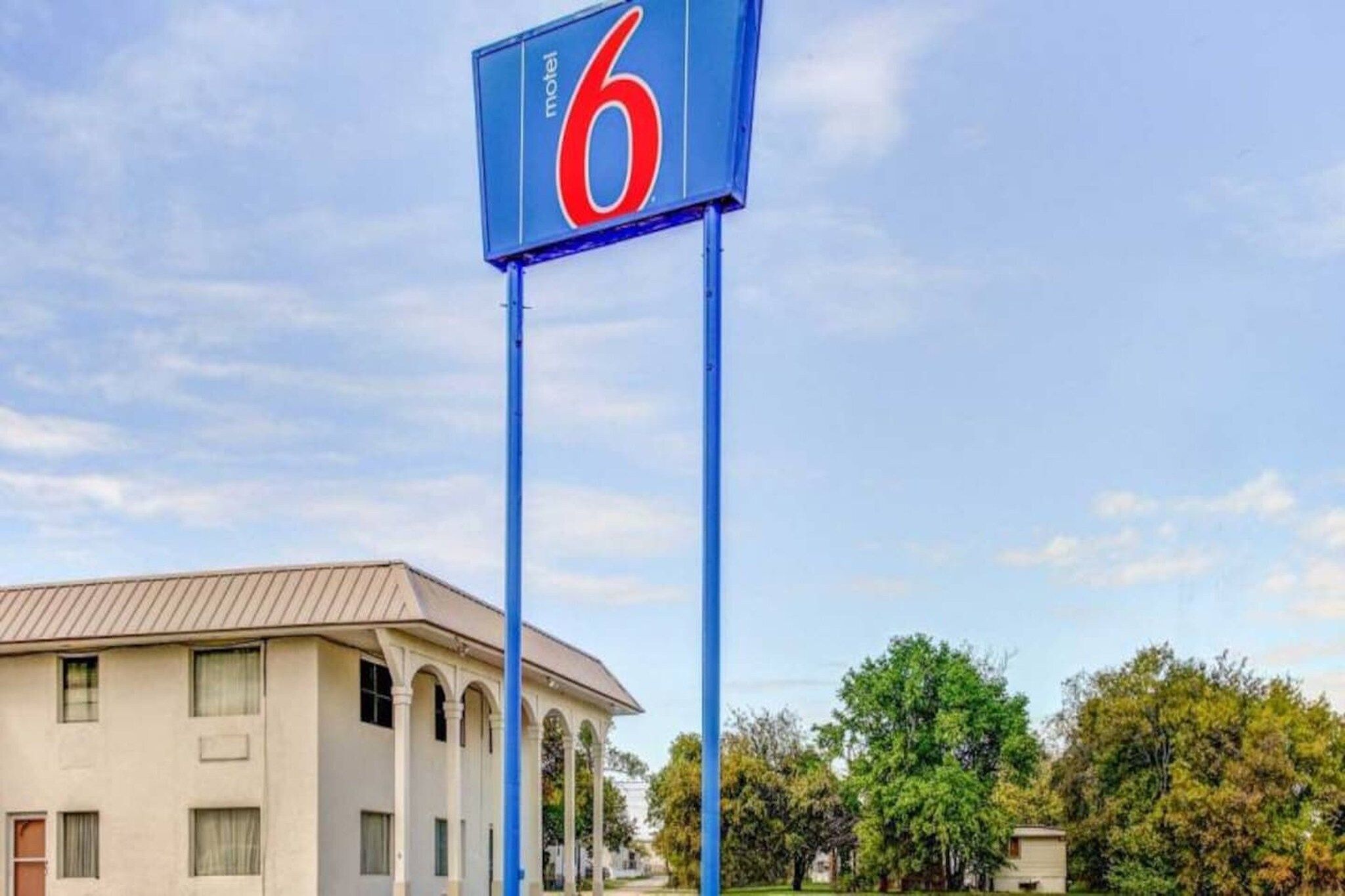 A motel sign with the number 6, a building with a beige facade and arched windows, and a clear sky.