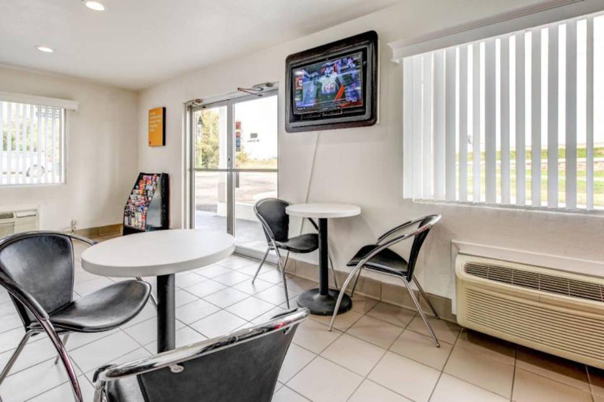 A hotel room with a large window, a flat-screen TV mounted on the wall, a small round table, and two chairs.