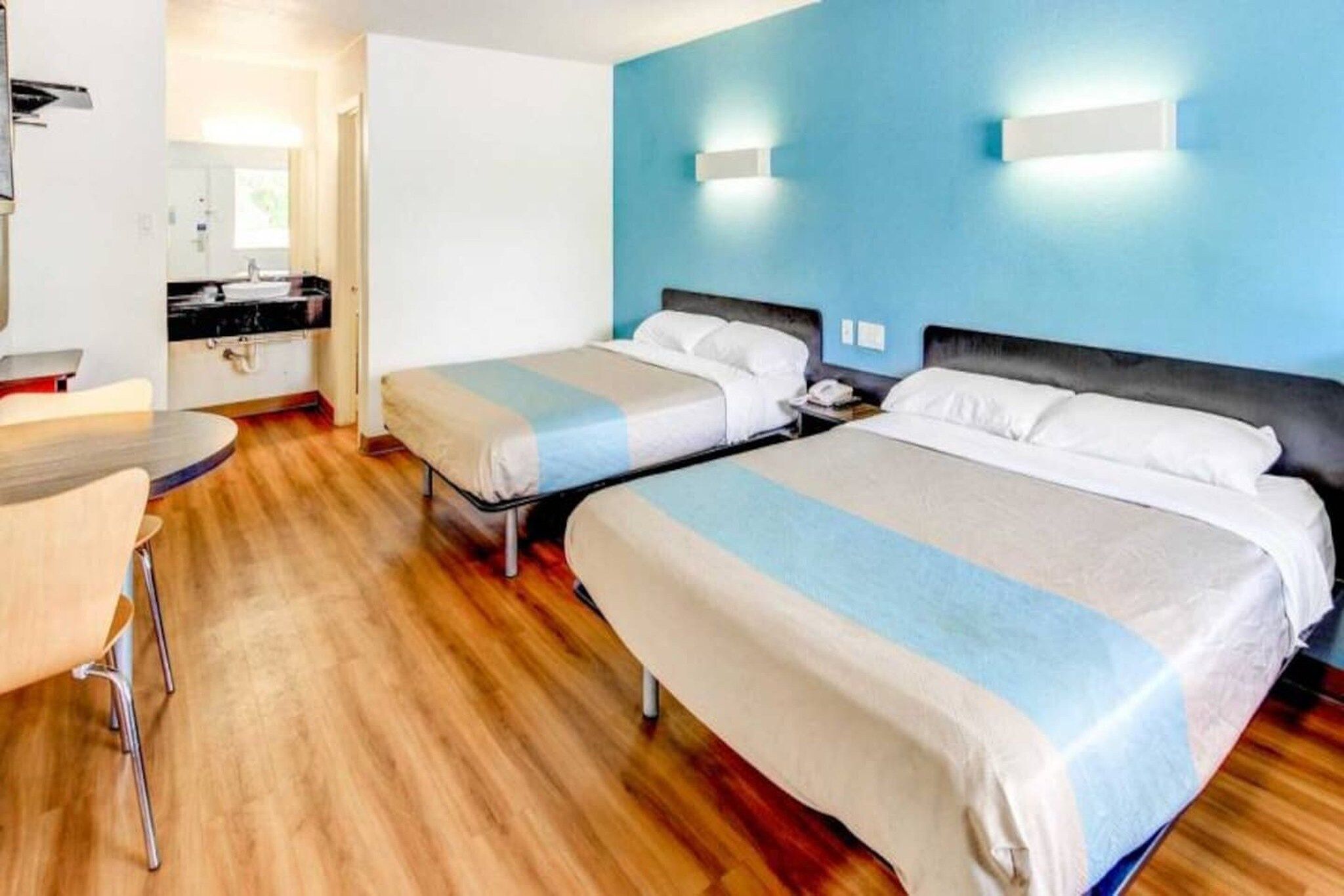 A hotel room with two beds, a desk, a chair, and a bathroom visible in the background.