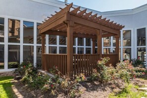 A wooden pergola structure with a slatted roof, surrounded by a garden with various plants and flowers. - 1 King Bed | Suite, Nsmk, Kitchen (Arlington)
