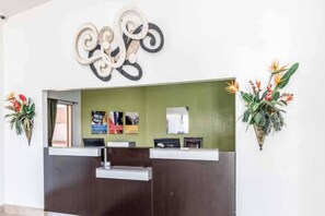 A reception desk with a green wall, a decorative wall piece, and two potted plants with tropical flowers. - 1 King Bed | Suite, Nsmk, Kitchen (Arlington)