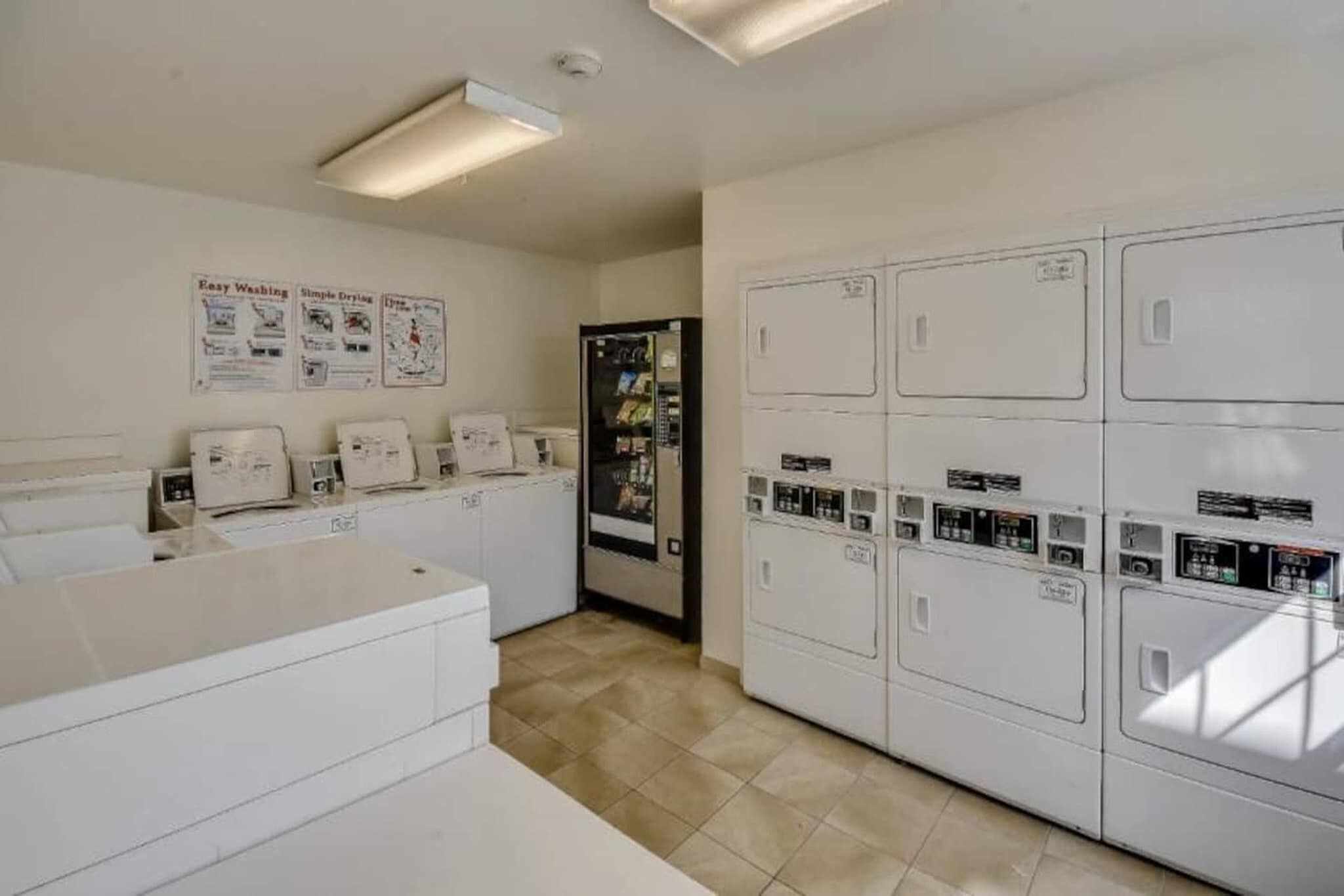 A laundry room with multiple washing machines and dryers, a refrigerator, and a tiled floor.