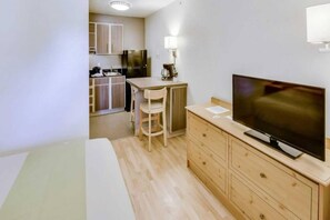 Kompakti hotellihuone, jossa on sänky, televisio, pieni työpöytä tuolilla, minikeittiö ja puinen kaappi.