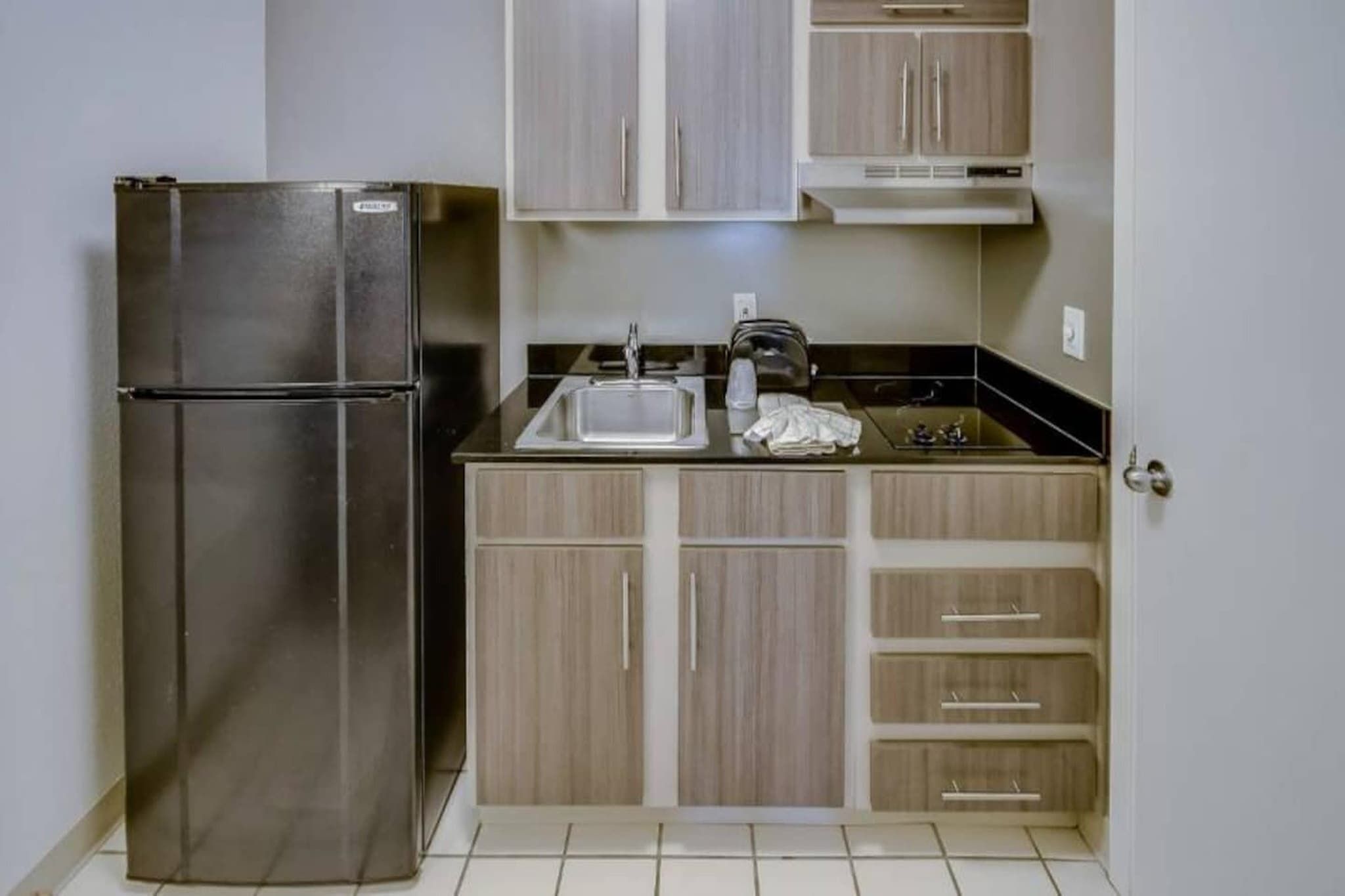 A compact kitchen with a stainless steel refrigerator, a sink, and wooden cabinets.