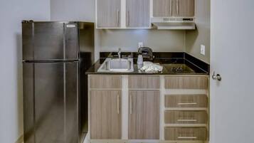 A compact kitchen with a stainless steel refrigerator, a sink, and wooden cabinets.