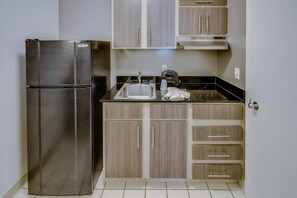 Una cocina compacta con un refrigerador de acero inoxidable, un lavamanos y armarios de madera.