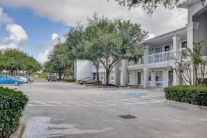 A parking lot with marked spaces, a building with a balcony, and trees. - 1 Queen Bed | ADA/Tub, Smoking (Houston)