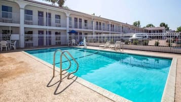 A swimming pool with a metal ladder, surrounded by a white fence, and a building with balconies in the background.
