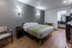 Ett hotellrum med en säng, en stol, ett skrivbord och en spegel.