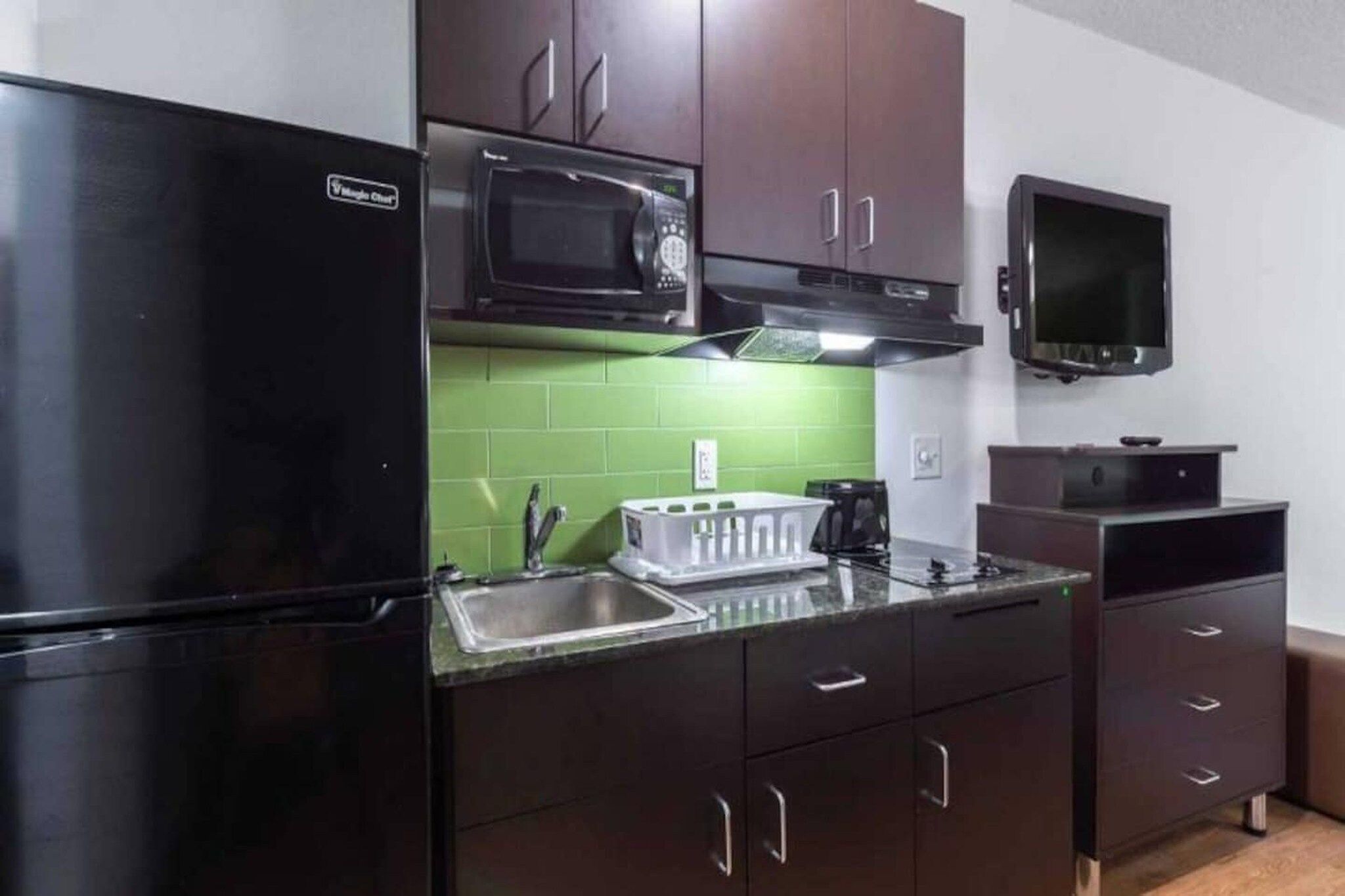 A compact kitchen with a black refrigerator, a microwave, a sink, and a small television.
