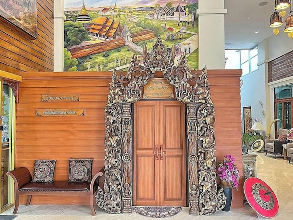 Una puerta de madera ornamentada con tallas intrincadas, un banco con cojines estampados y un mural que representa una escena tradicional.